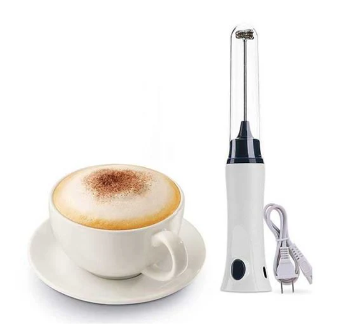White electric milk frother next to a cup of cappuccino on a white background